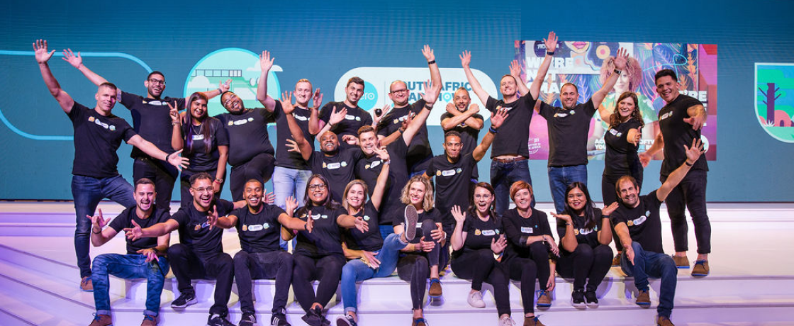 Large group of Xero staff wave at camera in front of large screen at Xero Roadshow